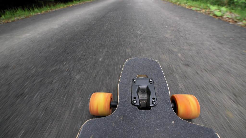 Longboard Skateboard with Orange Wheels Riding Downhill Asphalt Road POV
